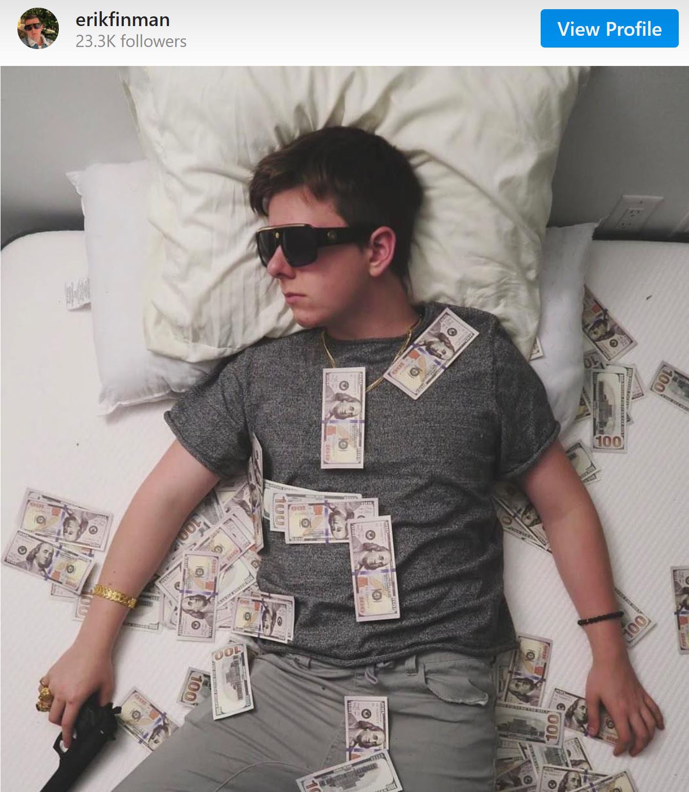 An Instagram post from Erik Finman, lying on a mattress holding a pistol, surrounded by cash. 